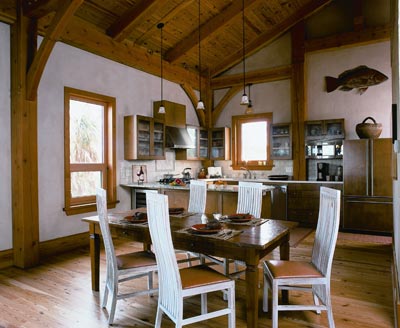 The warm, exposed wood of the timber framing defines the open plan of the kitchen and dining room, which flows into the gathering room. Rich maple cabinets in the kitchen are fronted with seeded glass. Stainless steel, energy-efficient appliances lend a contemporary accent to the abundance of wood.